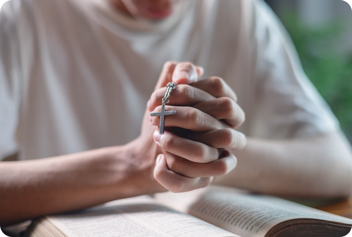 Person clasping cross necklace in prayer